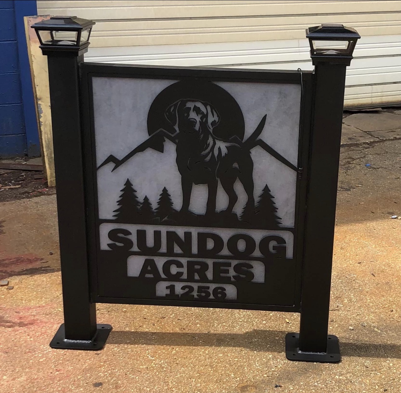 Sign with a dog silhouette, mountains, trees, and text reading 'Sundog Acres 1256'.