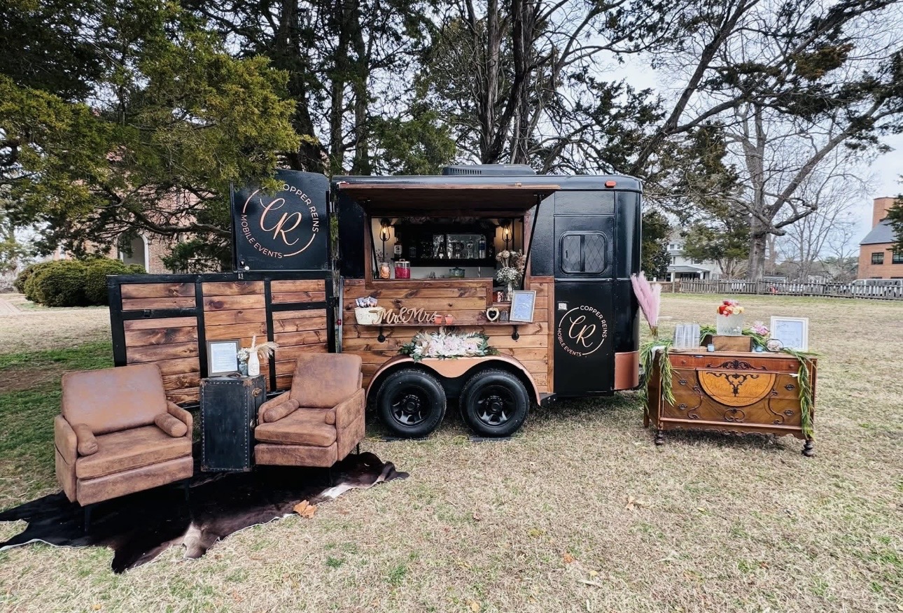 Food truck with seating area and decorative chest outdoors on grass, trees in background, daytime.
