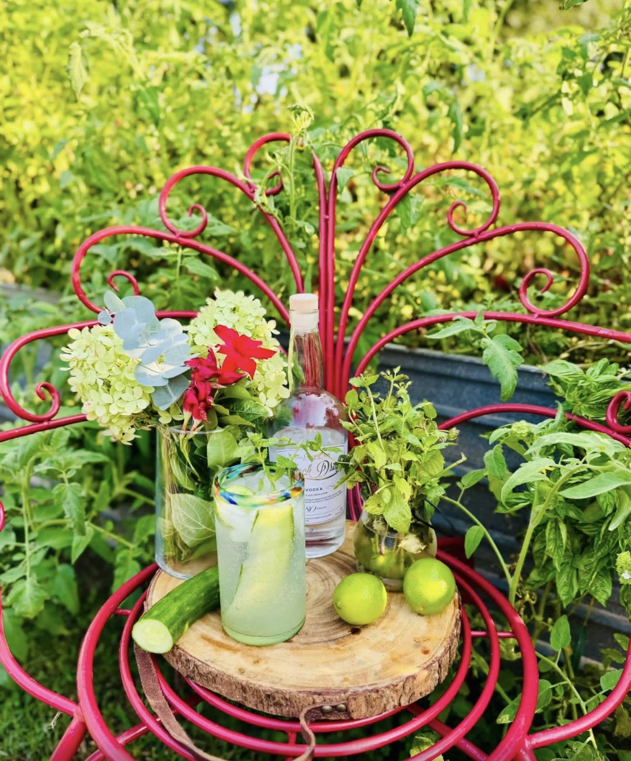 Pink decorative metal chair with a wooden seat holding jars, green apples, and plants, outdoors with green foliage background.