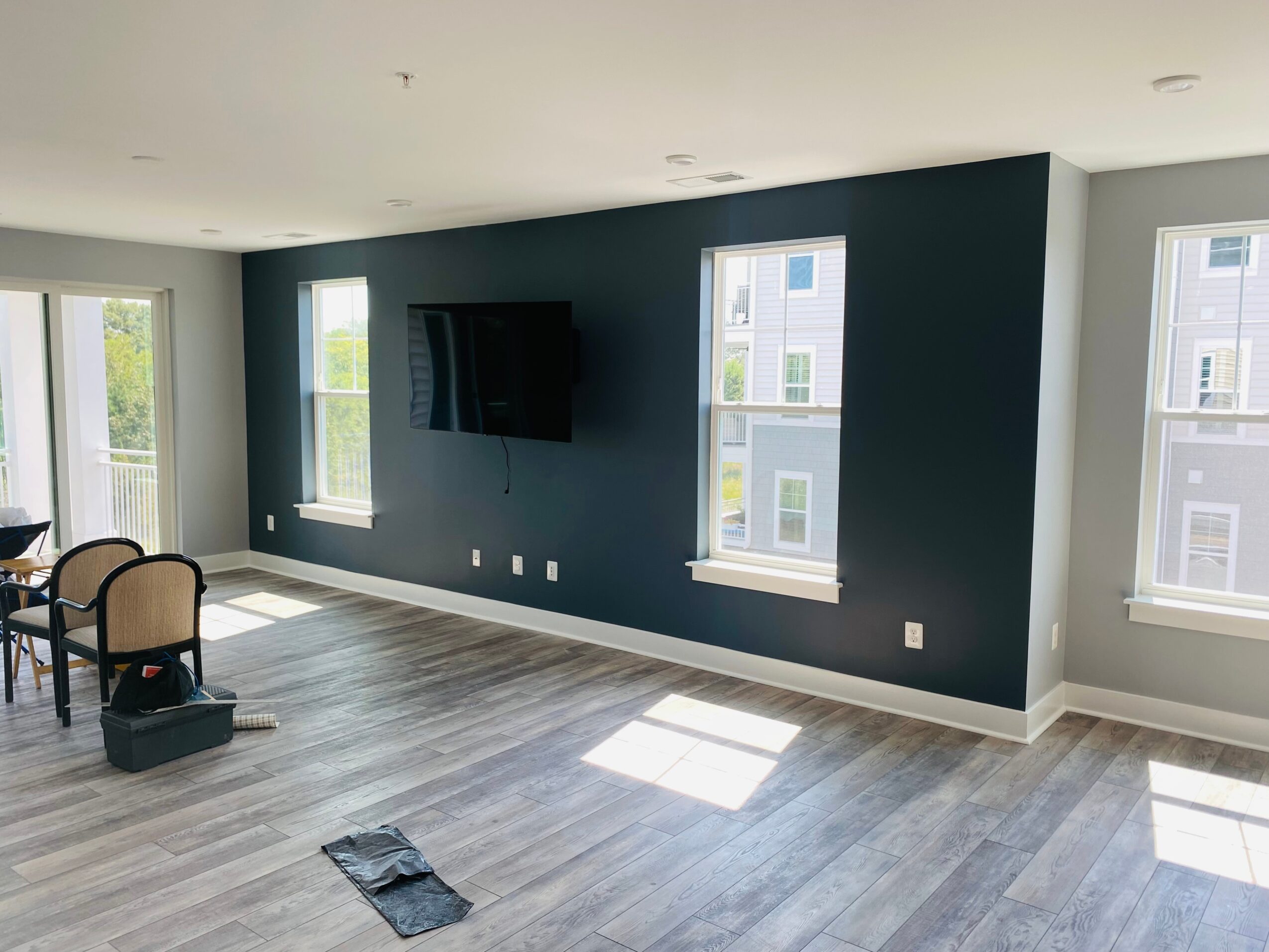 Living room with dark blue accent wall, three windows, a wall-mounted TV, and light-colored flooring.