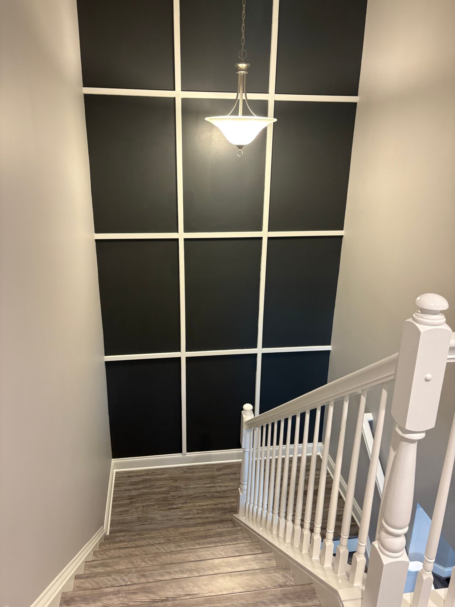 Room corner with black wall panels, a white lamp, and a white railing, with wooden flooring and a white wall.