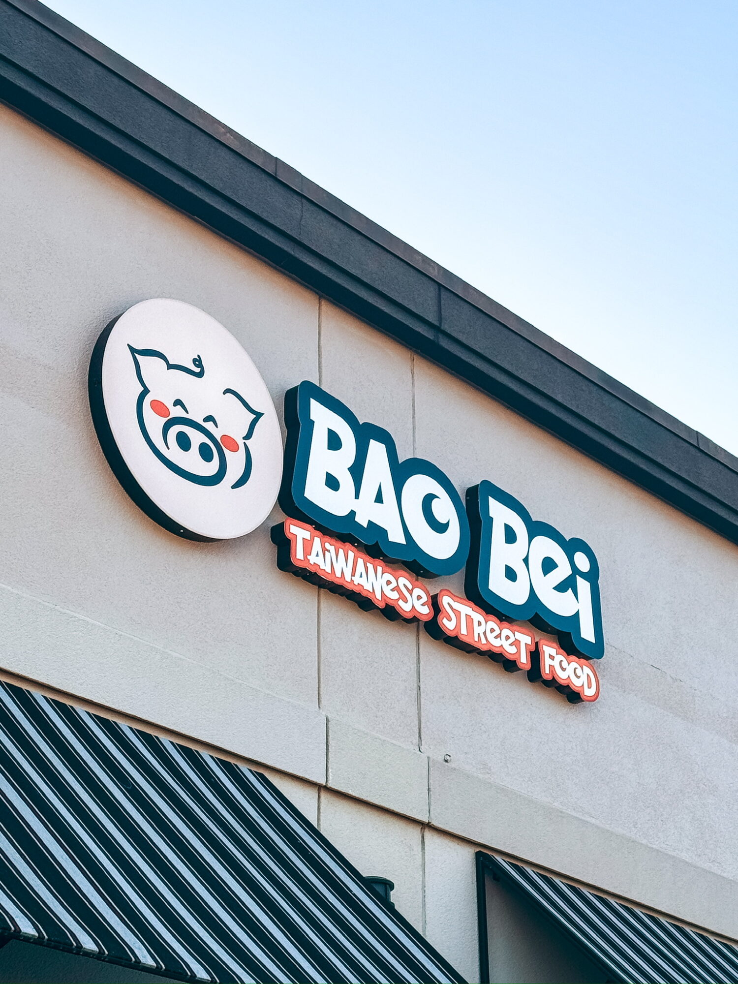 Sign for Bao Bei restaurant with a pig logo and text, on a building exterior, against a clear sky.