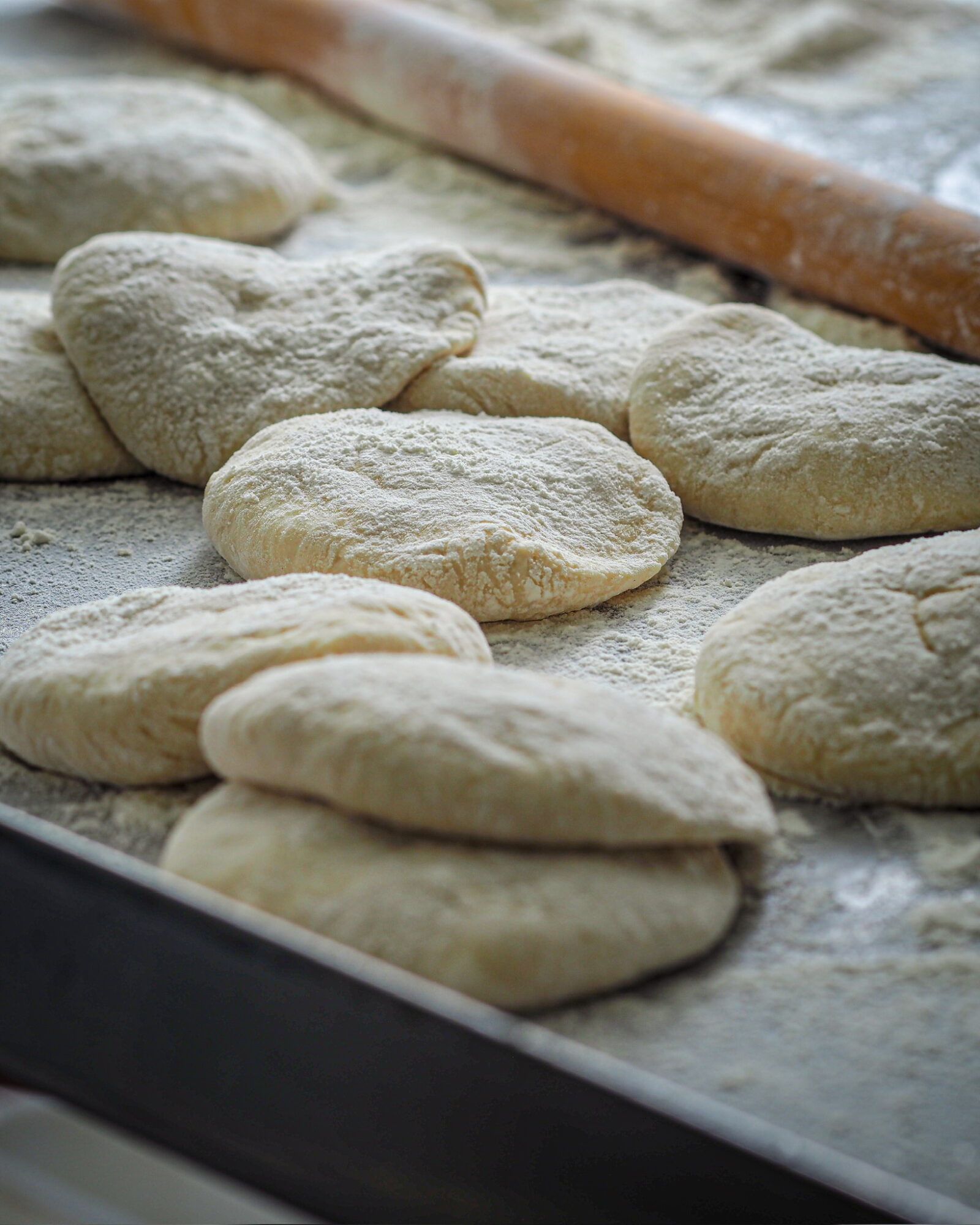 Unbaked bread dough shaped into various forms on a floured surface with a rolling pin nearby.
