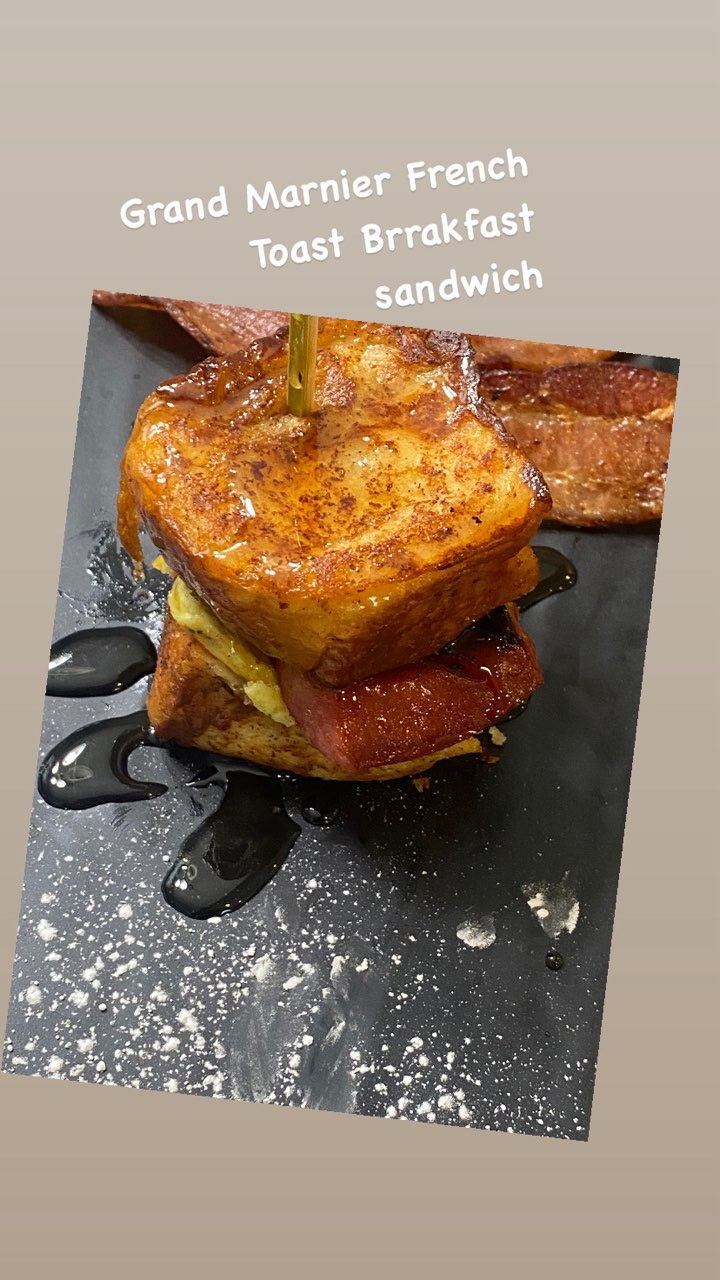 Stacked French toast with syrup and bacon on a black plate, sprinkled with powdered sugar.