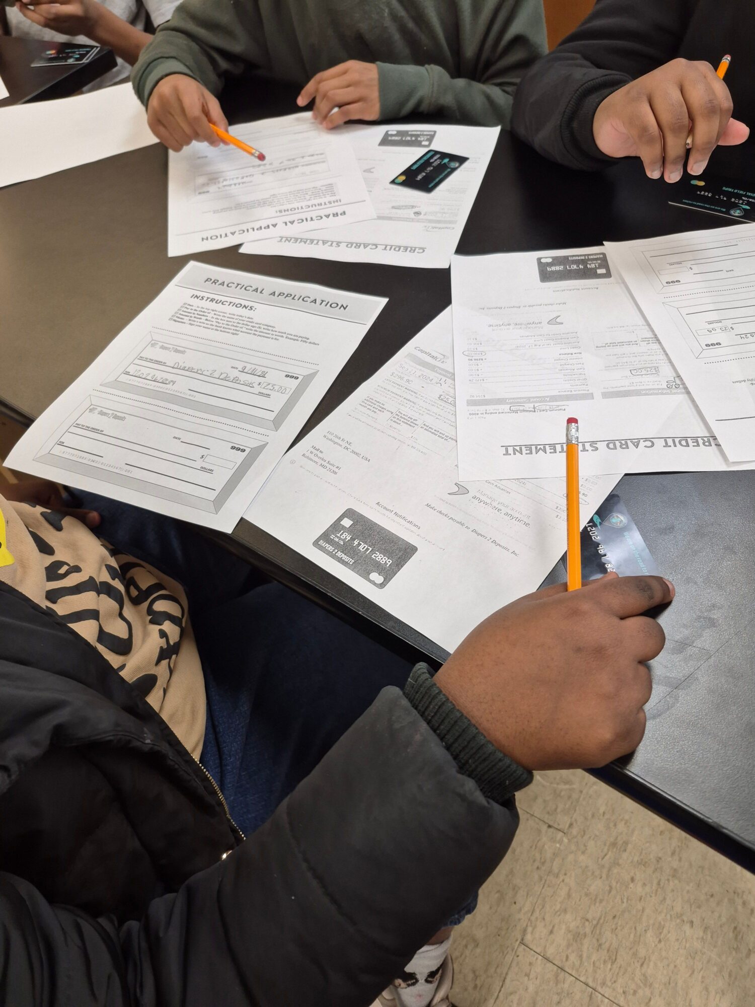 Two people at a table working on documents, one holding a pencil, papers spread out, and a laptop partially visible.