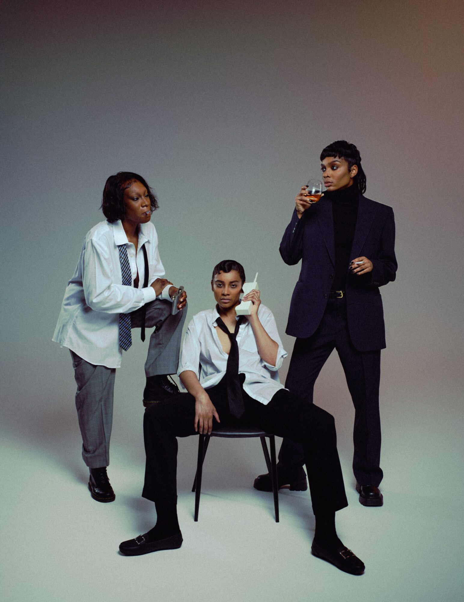 Three people, two women and one man, pose with drinks against a plain background.