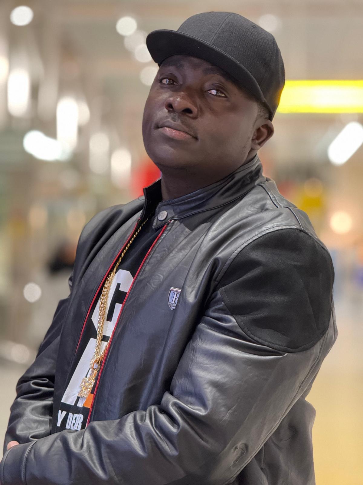 Young man wearing a black cap and leather jacket, looking slightly upward in an indoor setting.