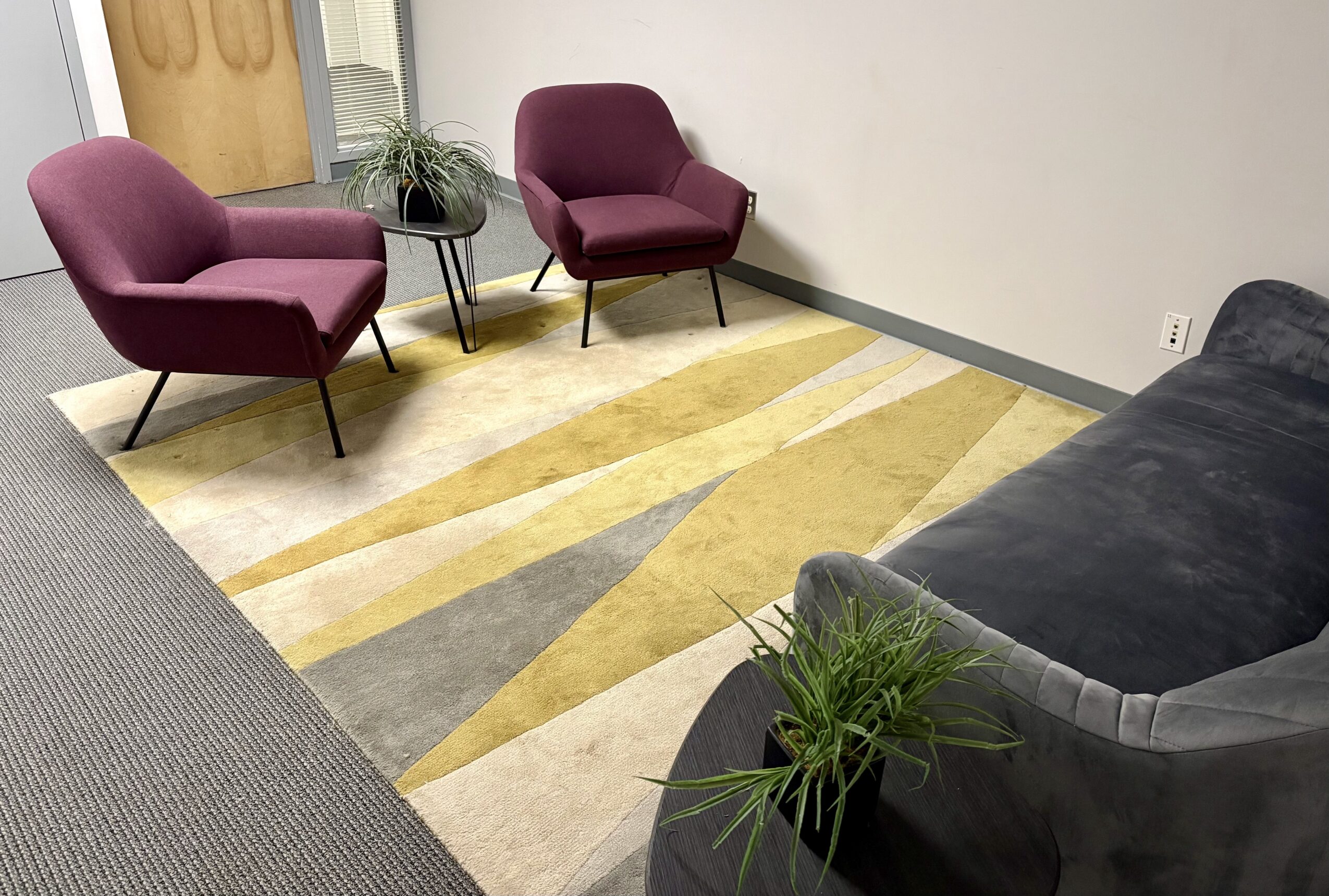 Two purple armchairs, a gray sofa, and a small table with a plant in a room with a patterned rug.