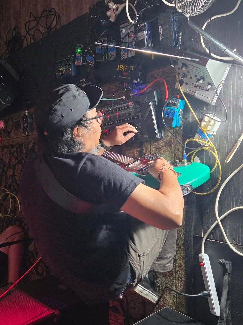 Person wearing a cap and black shirt working with electronic equipment on a table, viewed from above.