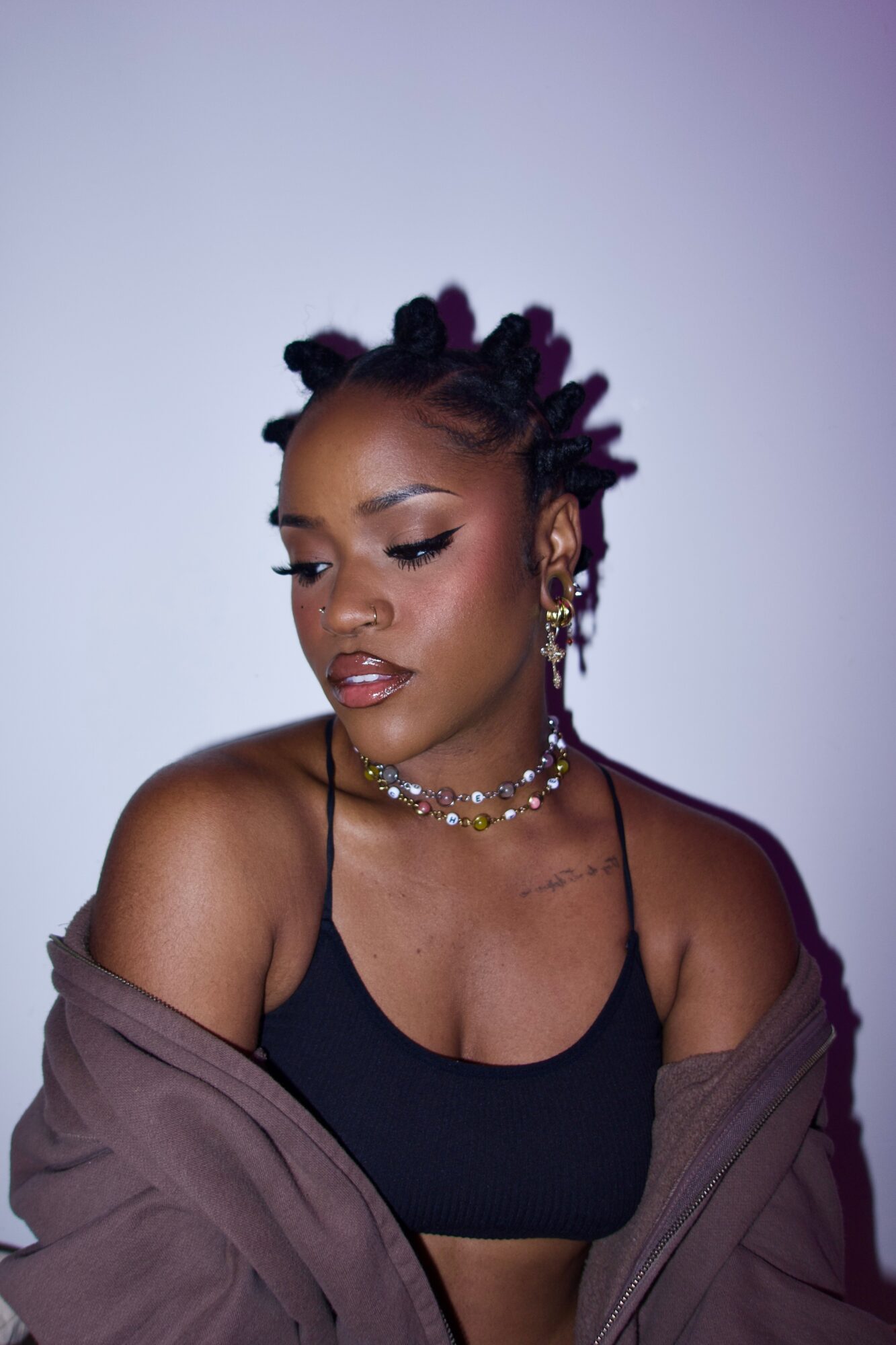 Young woman with styled hair, wearing jewelry and a black top, looking down with a neutral expression.