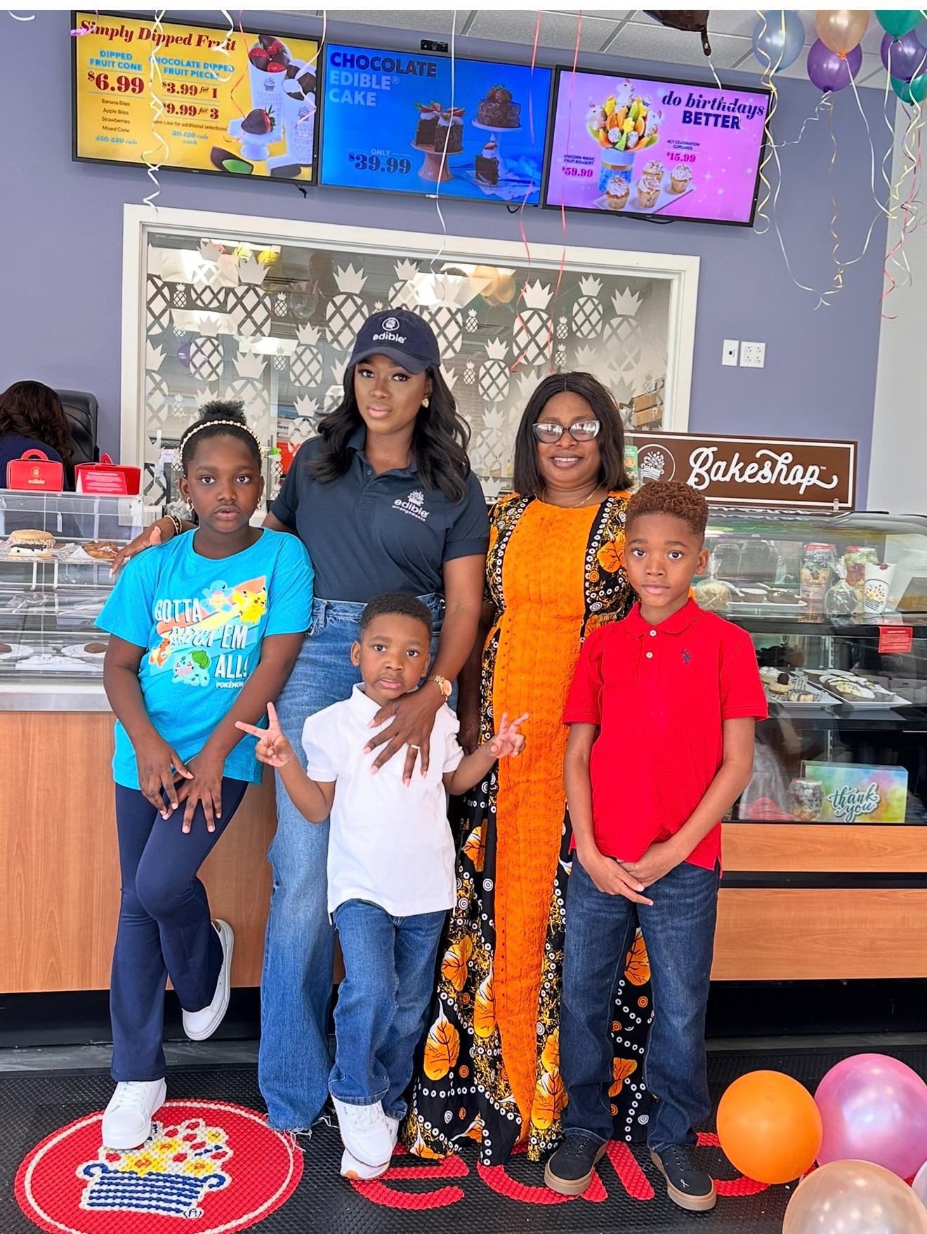 Four people, two children and two adults, stand inside a bakery or cake shop, smiling at the camera.