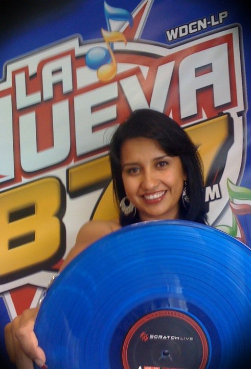 Smiling woman holding a blue vinyl record in front of a colorful radio station logo background.