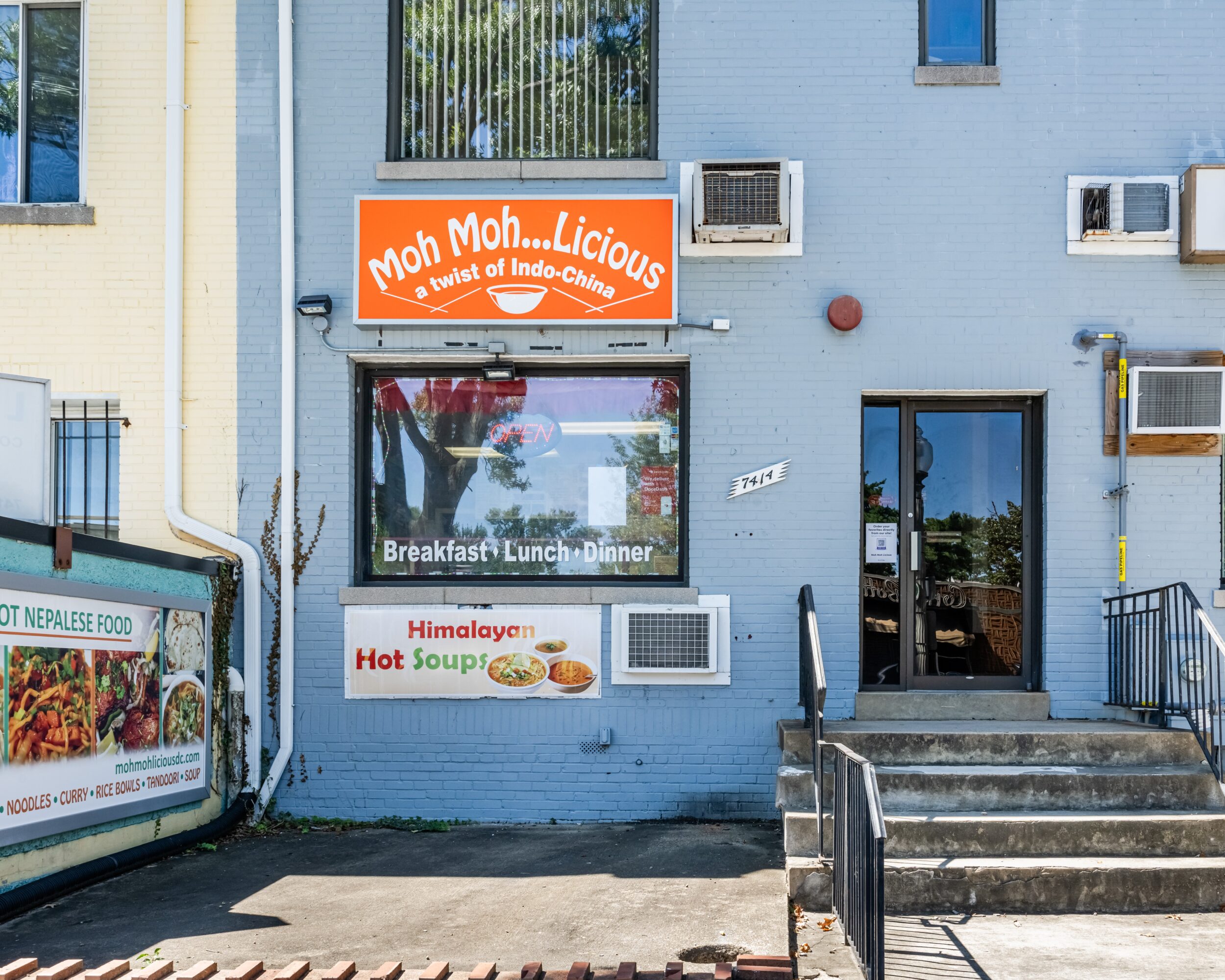 Blue building with signs advertising Indian cuisine, breakfast, lunch, dinner, and hot soup, with stairs leading to a door.