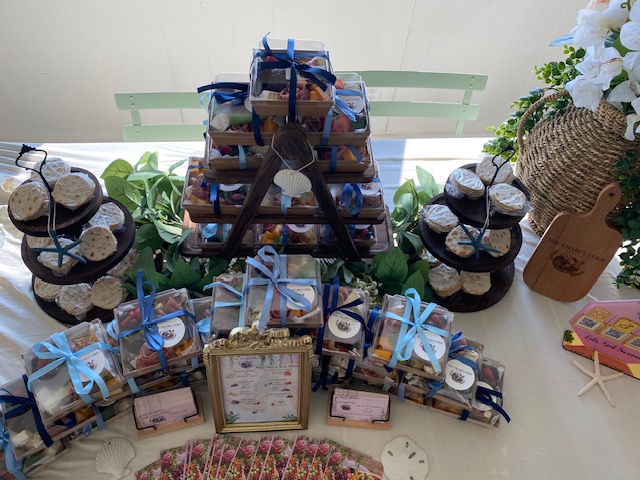 Display of small jars with blue ribbons, a framed sign, and decorative items on a table, with a basket of white flowers nearby.