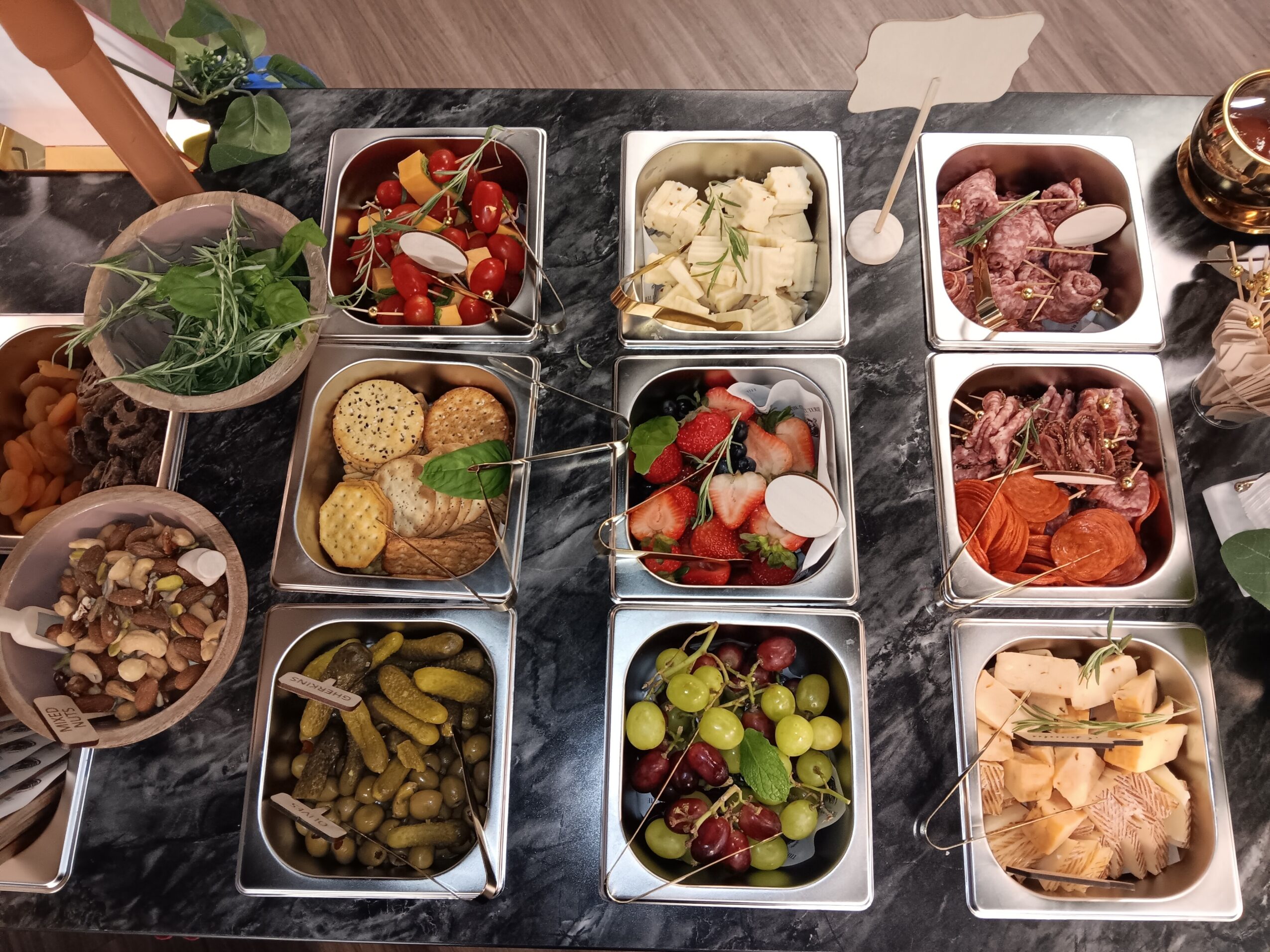 Assorted dishes including salads, cheeses, fruits, and meats on a table, with bowls and plates arranged neatly.
