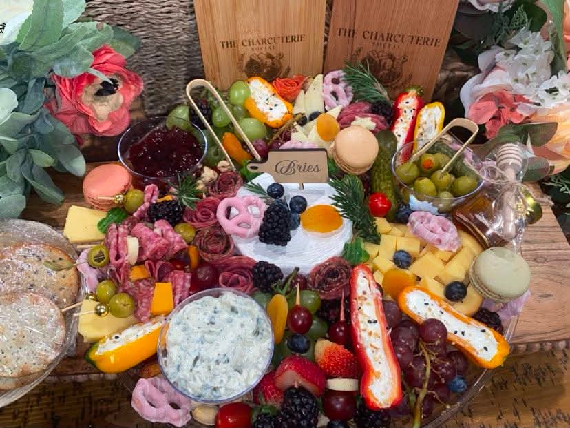 Decorative cake surrounded by fruits, candies, and flowers on a table.