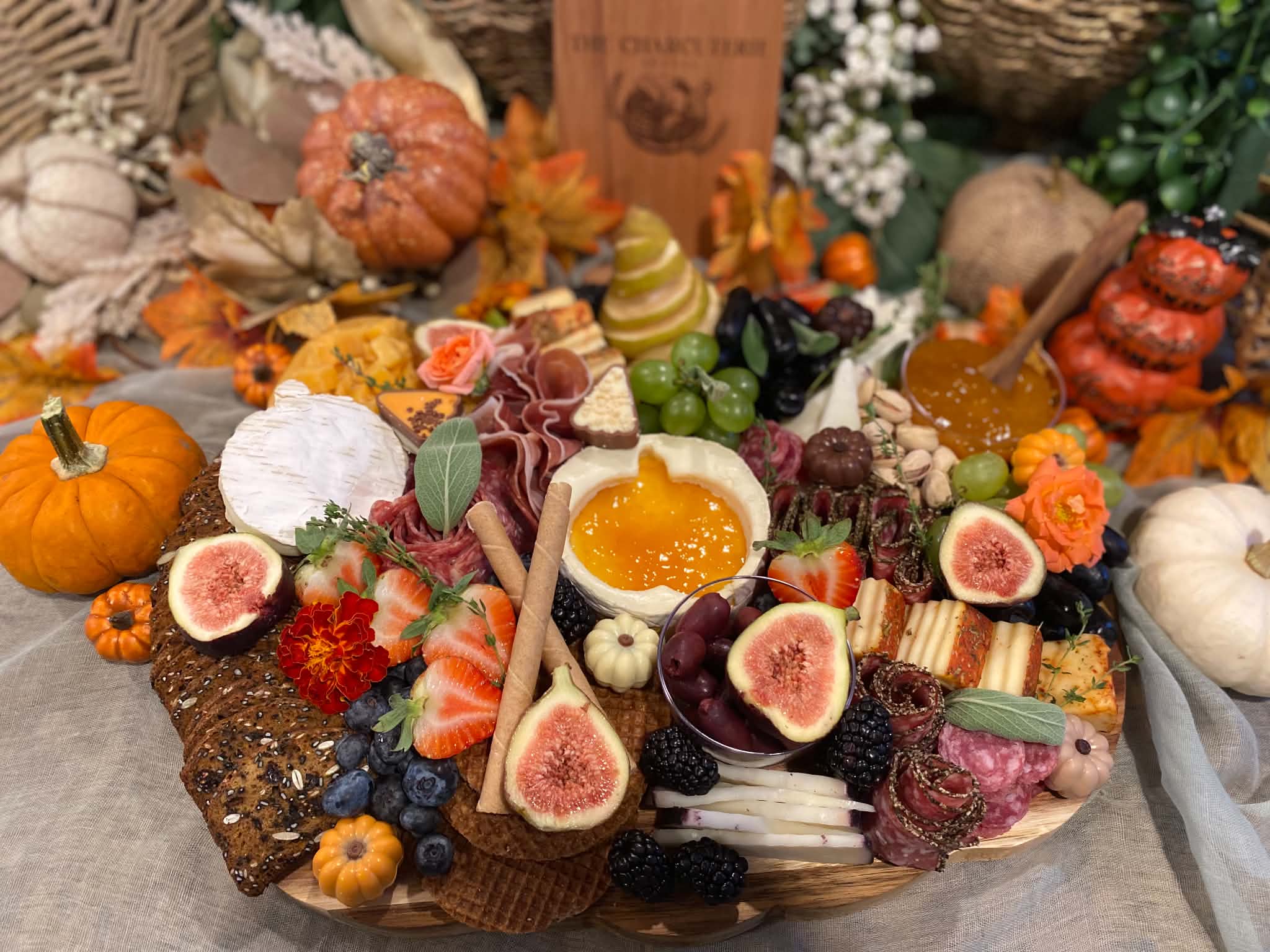 Assorted fruits, vegetables, and decorative items arranged on a table with pumpkins, flowers, and gourds.