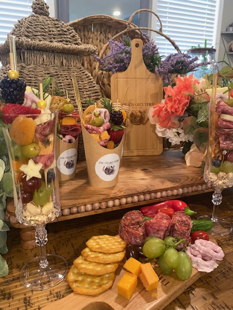 Table with fruit, cheese, and snacks, decorated with flowers and candles, in a cozy room with wicker furniture.