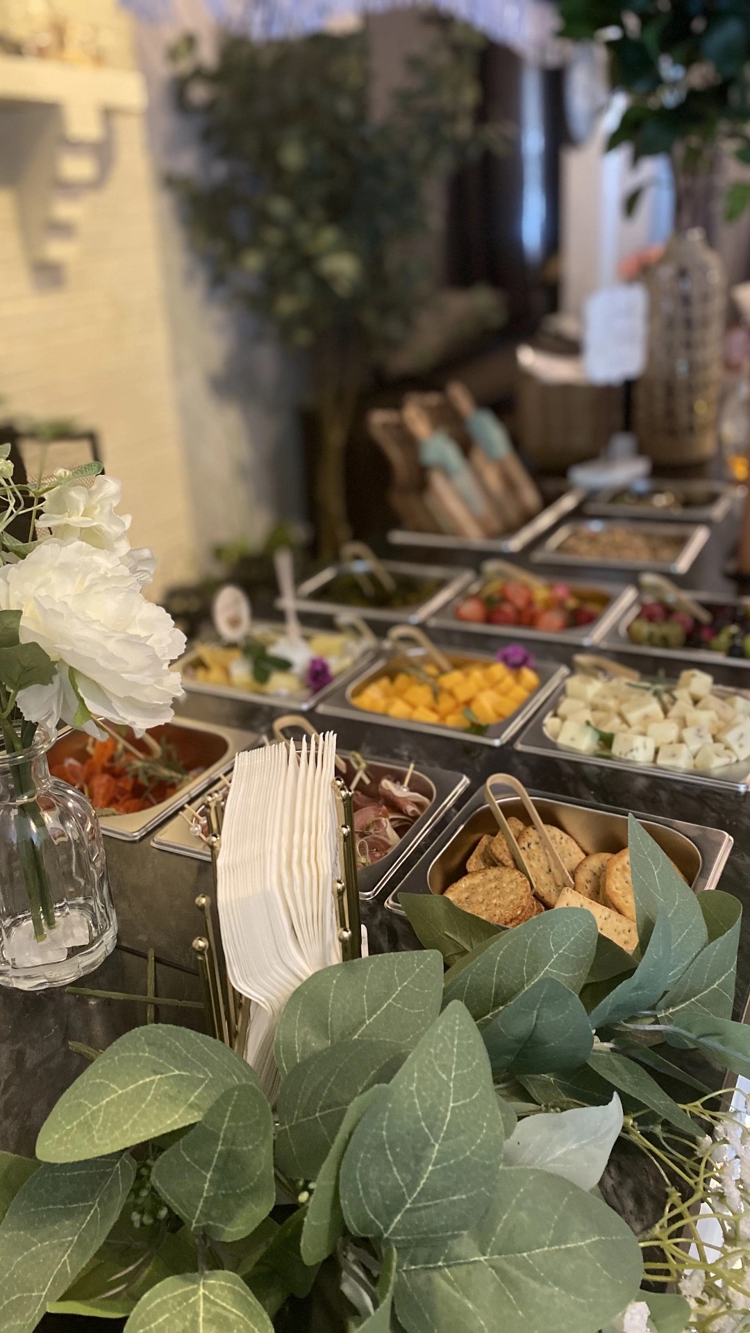 Buffet table with various dishes, flowers, and greenery, set in an indoor space with decorative elements.