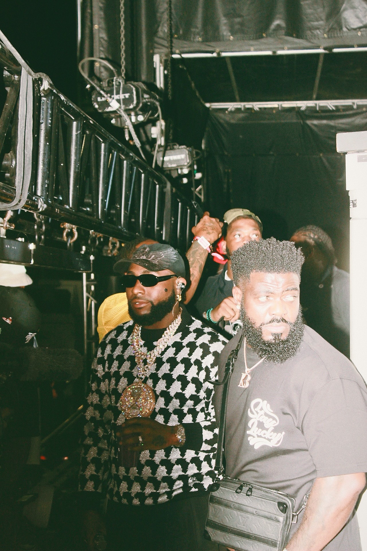 Group of people in a backstage area with equipment, some looking at the camera, others engaged elsewhere.