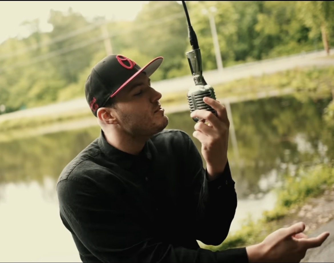 Person holding a radio device outdoors near a body of water, with trees in the background.