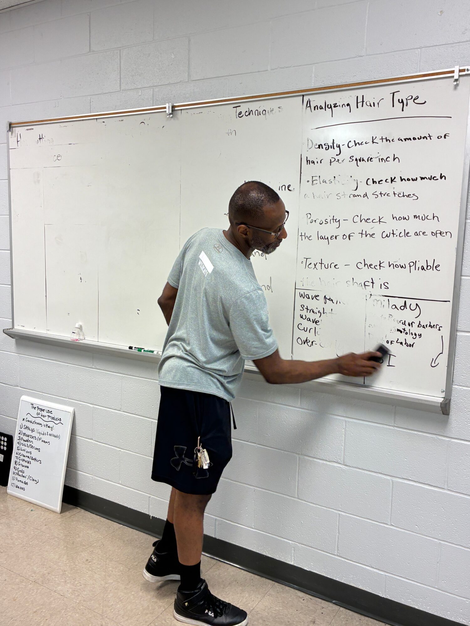 Person writing on a whiteboard with text and notes, standing in a room with tiled walls.