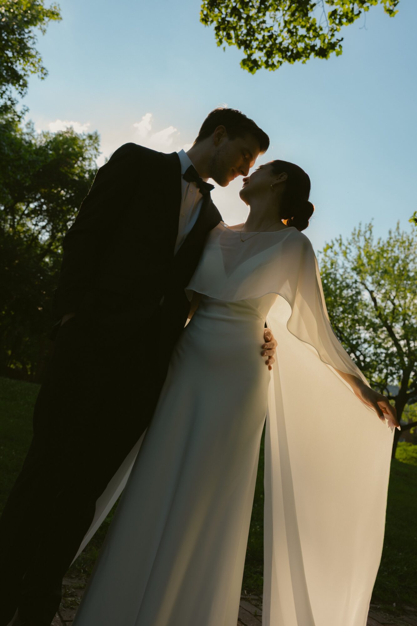 Silhouette of a couple outdoors, facing each other, with trees and sky in the background.