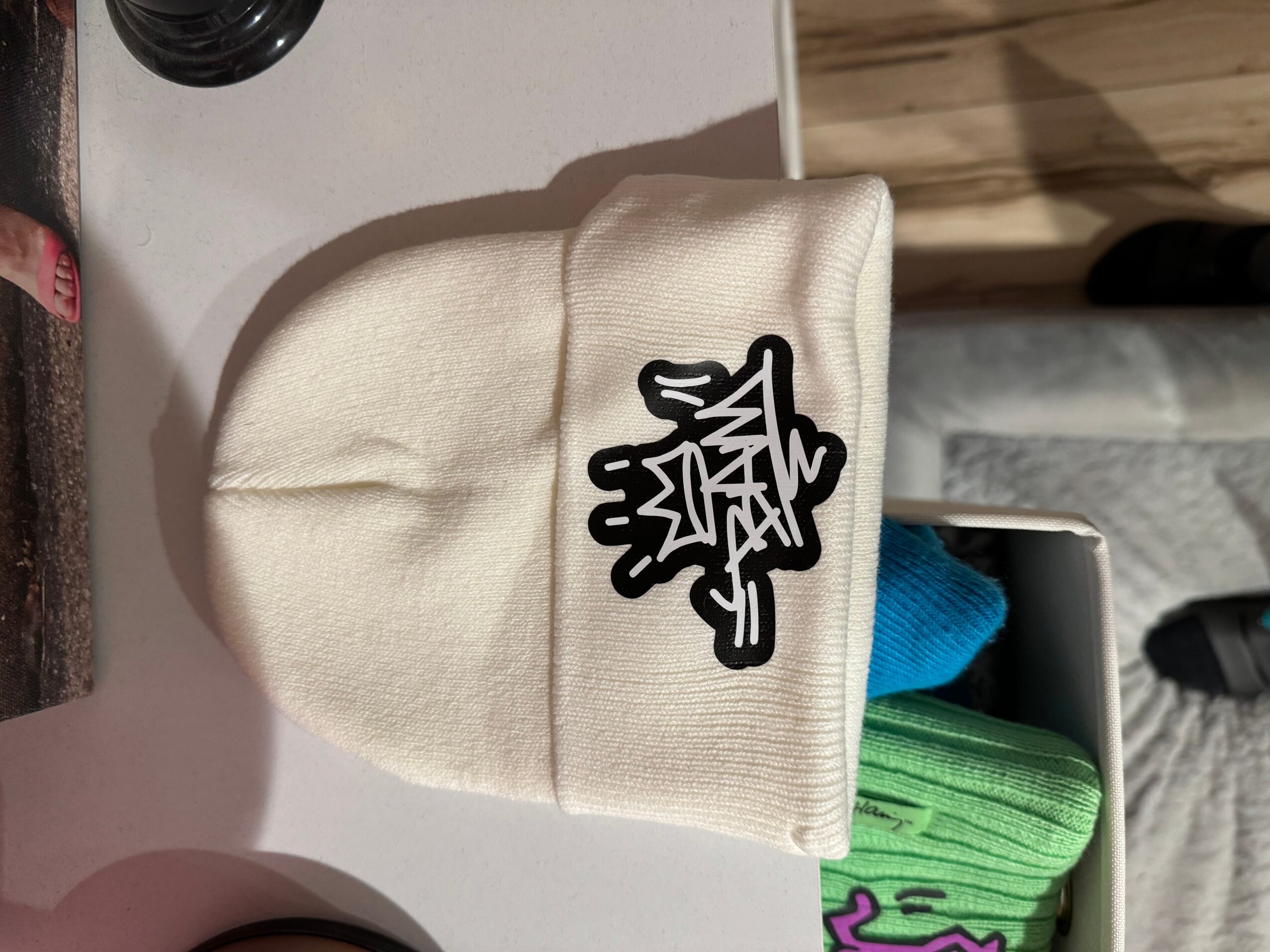 Cream-colored beanie with a black and white patch, placed on a surface with a blue and green object nearby.
