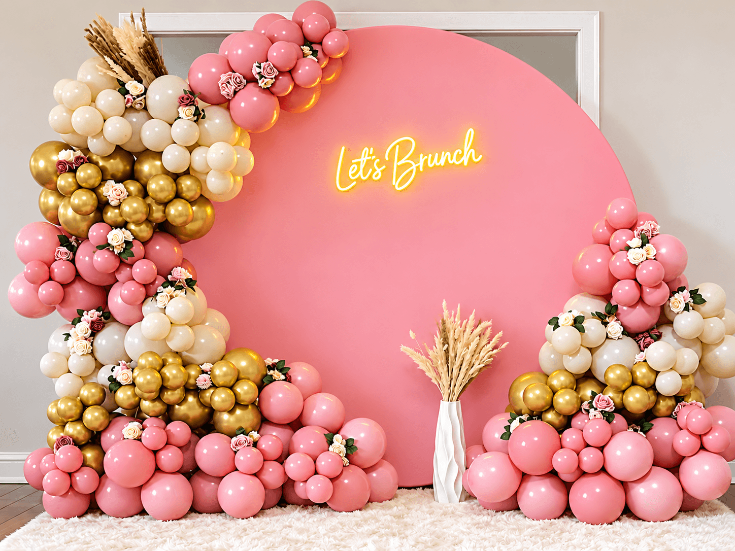 Decorative pink, white, and gold balloons arranged around a pink backdrop with a yellow neon sign that says