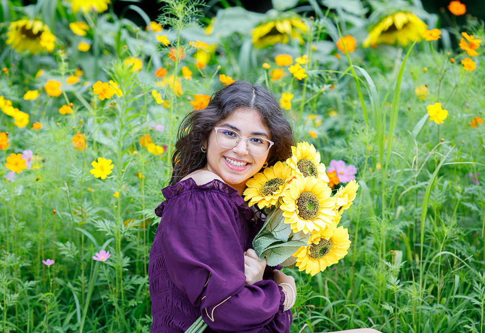 Young girl with glasses holding a bouquet of sunflowers in a colorful flower field.