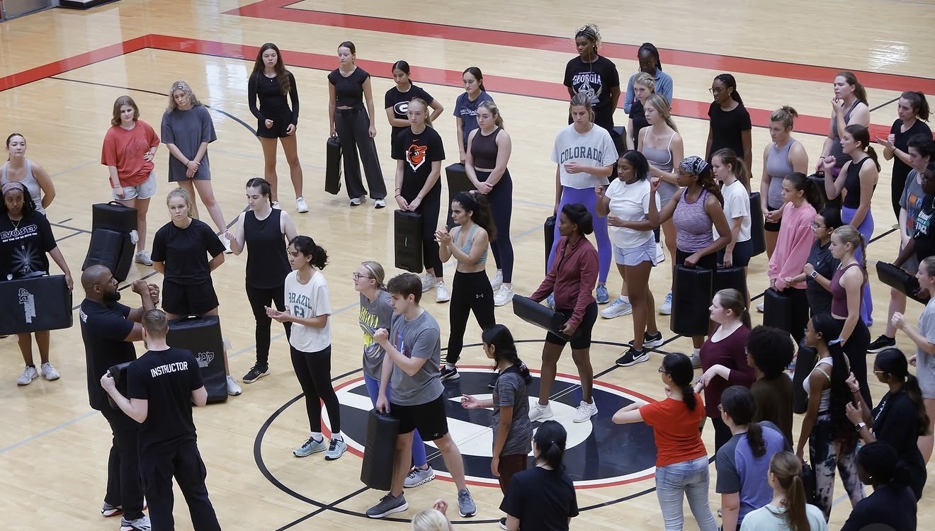Group of people standing and walking on a gymnasium floor during an indoor event.