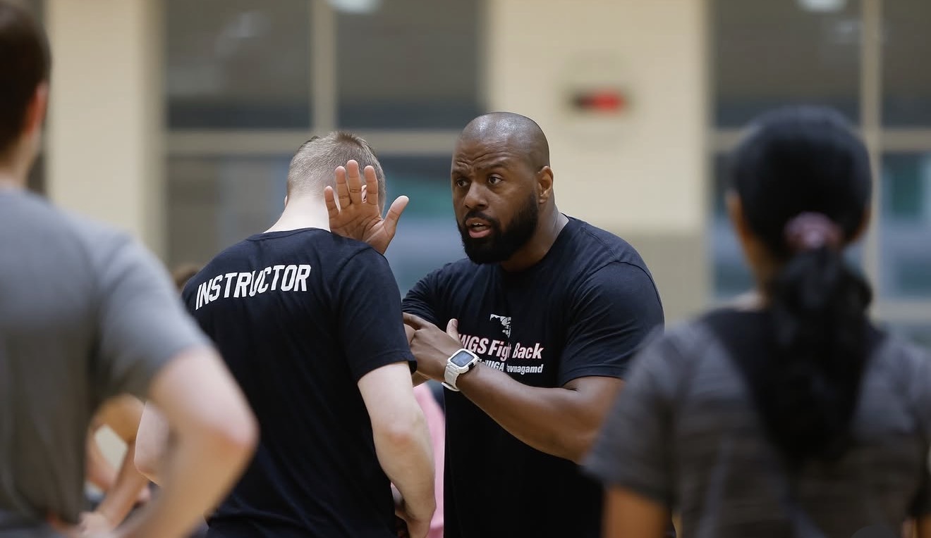 Coach speaking to athletes during a training session, with a gym or sports facility in the background.