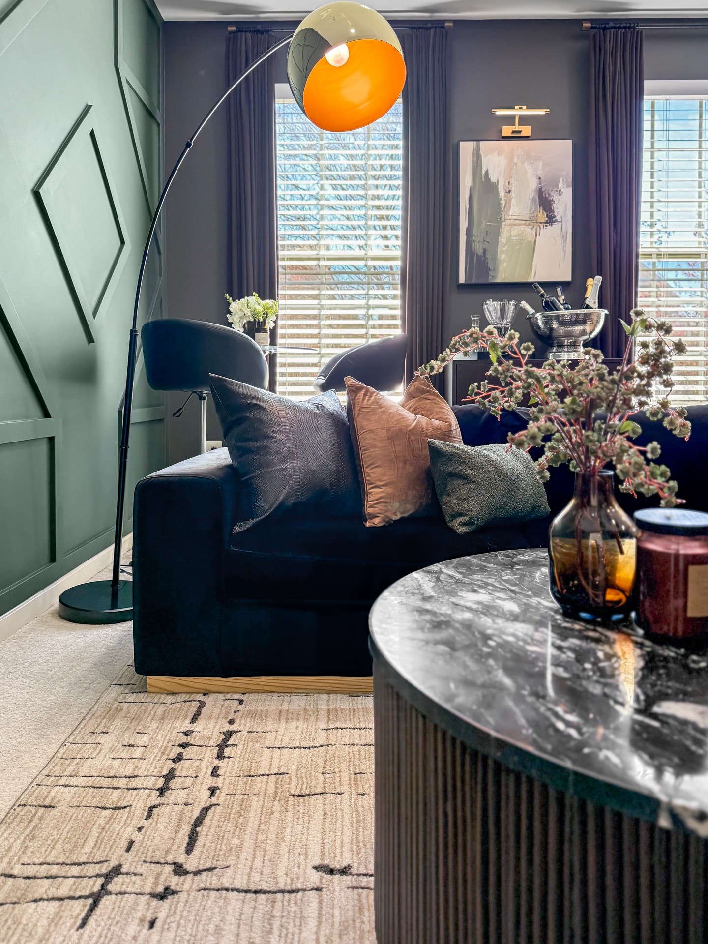 Living room with dark sofa, marble table, floral arrangement, and large window with curtains.