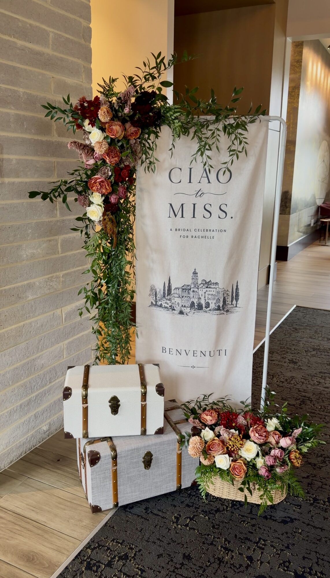 Flower arrangement with pink, red, and white flowers, a white sign with text and a city illustration, and vintage suitcases.
