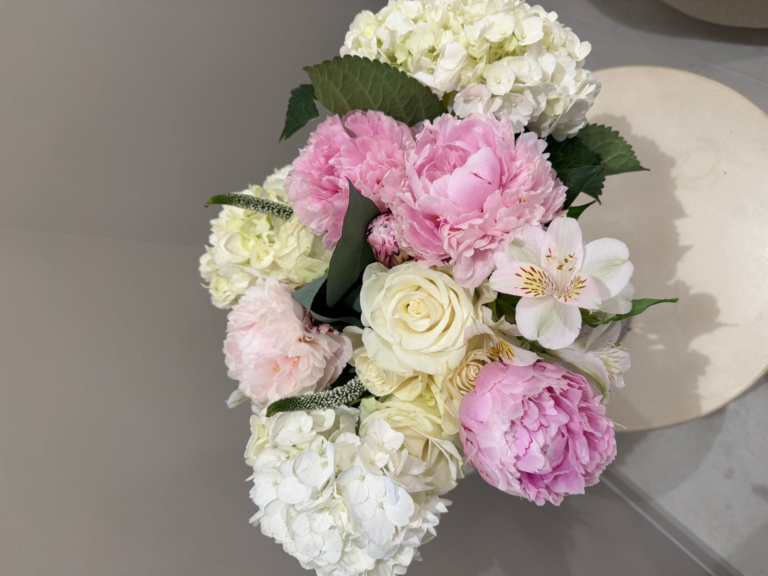 Flower arrangement with white, pink, and cream flowers, including roses and peonies, on a gray surface.