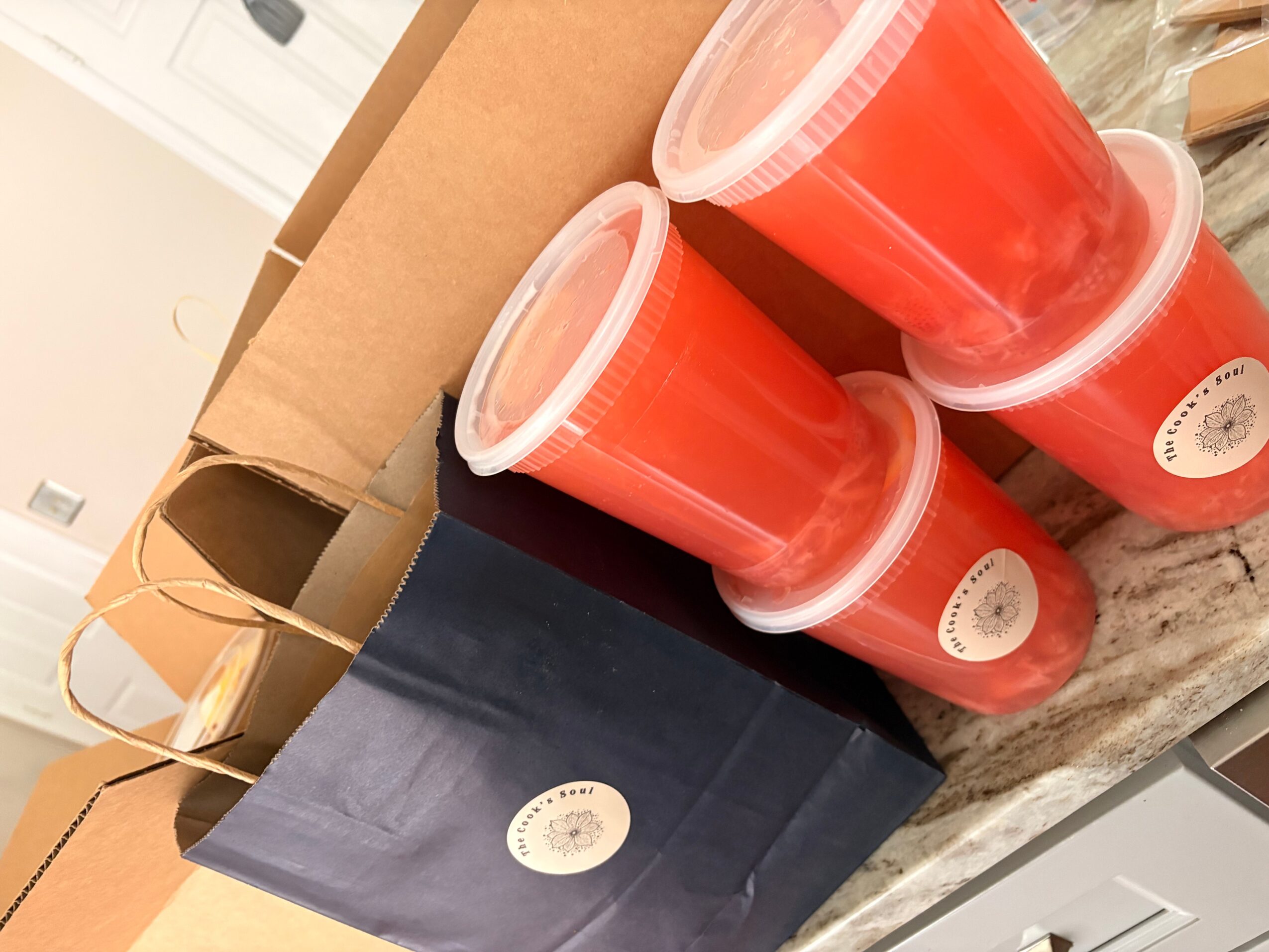 Four red cups with clear lids on a marble surface, with a cardboard box and a black bag nearby.