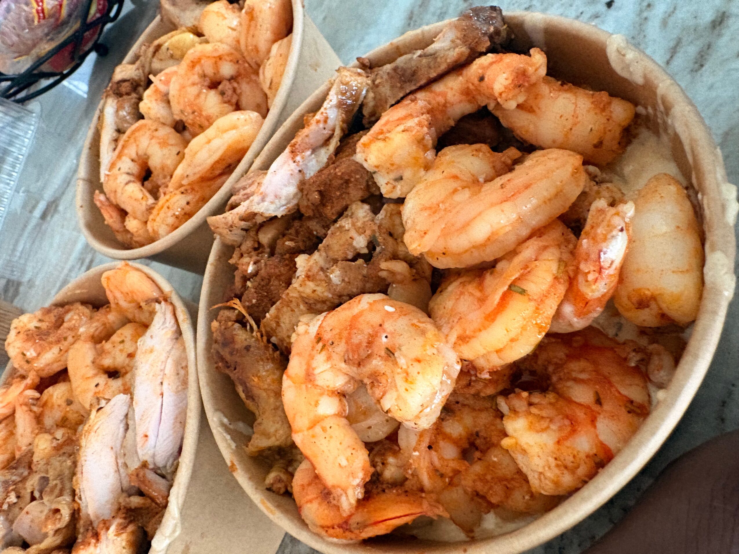 Three bowls filled with cooked shrimp and fried fish on a table, viewed from above.