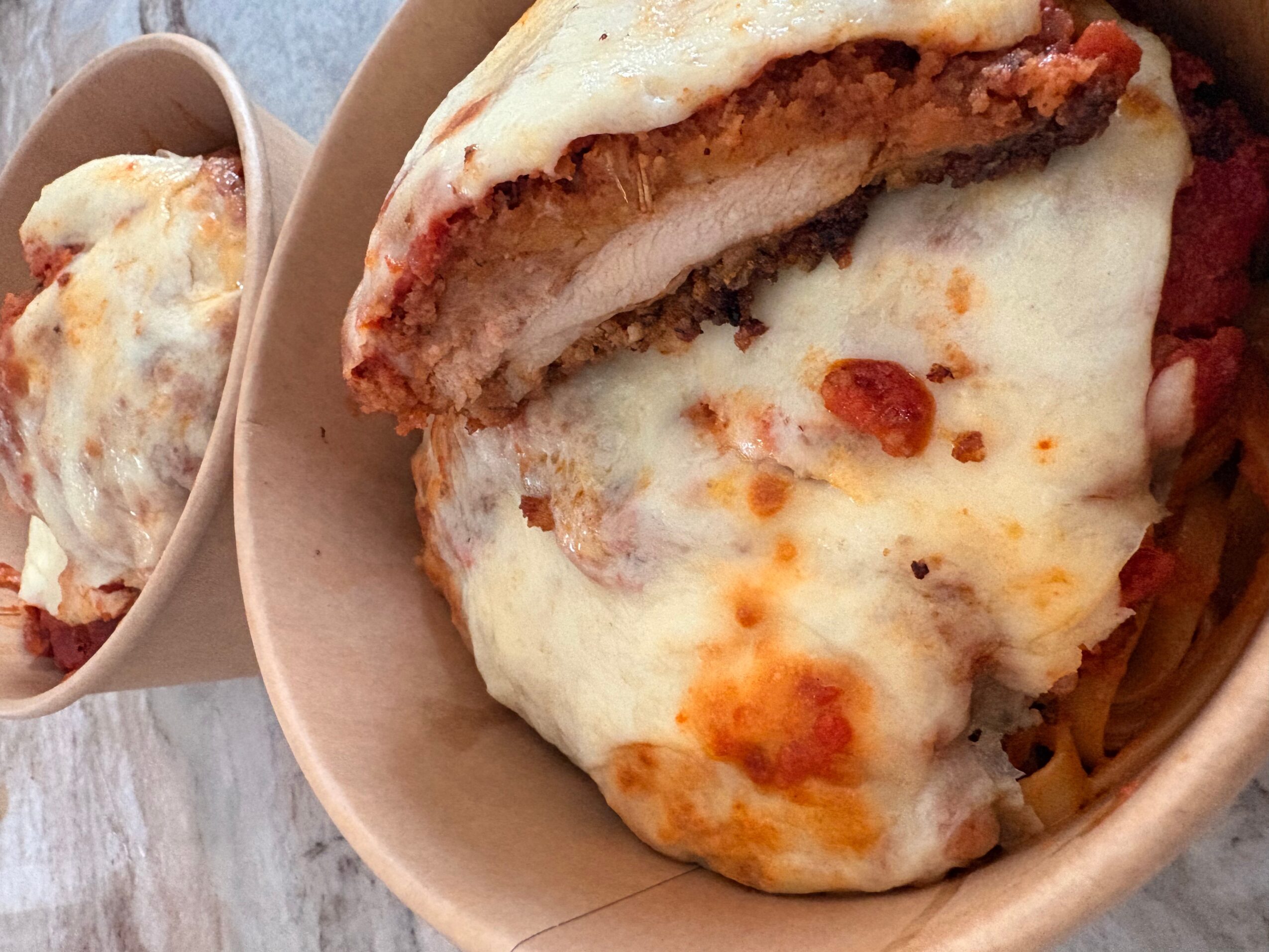 Close-up of a baked pasta dish with melted cheese, tomato sauce, and a breaded meat patty, served in a bowl.