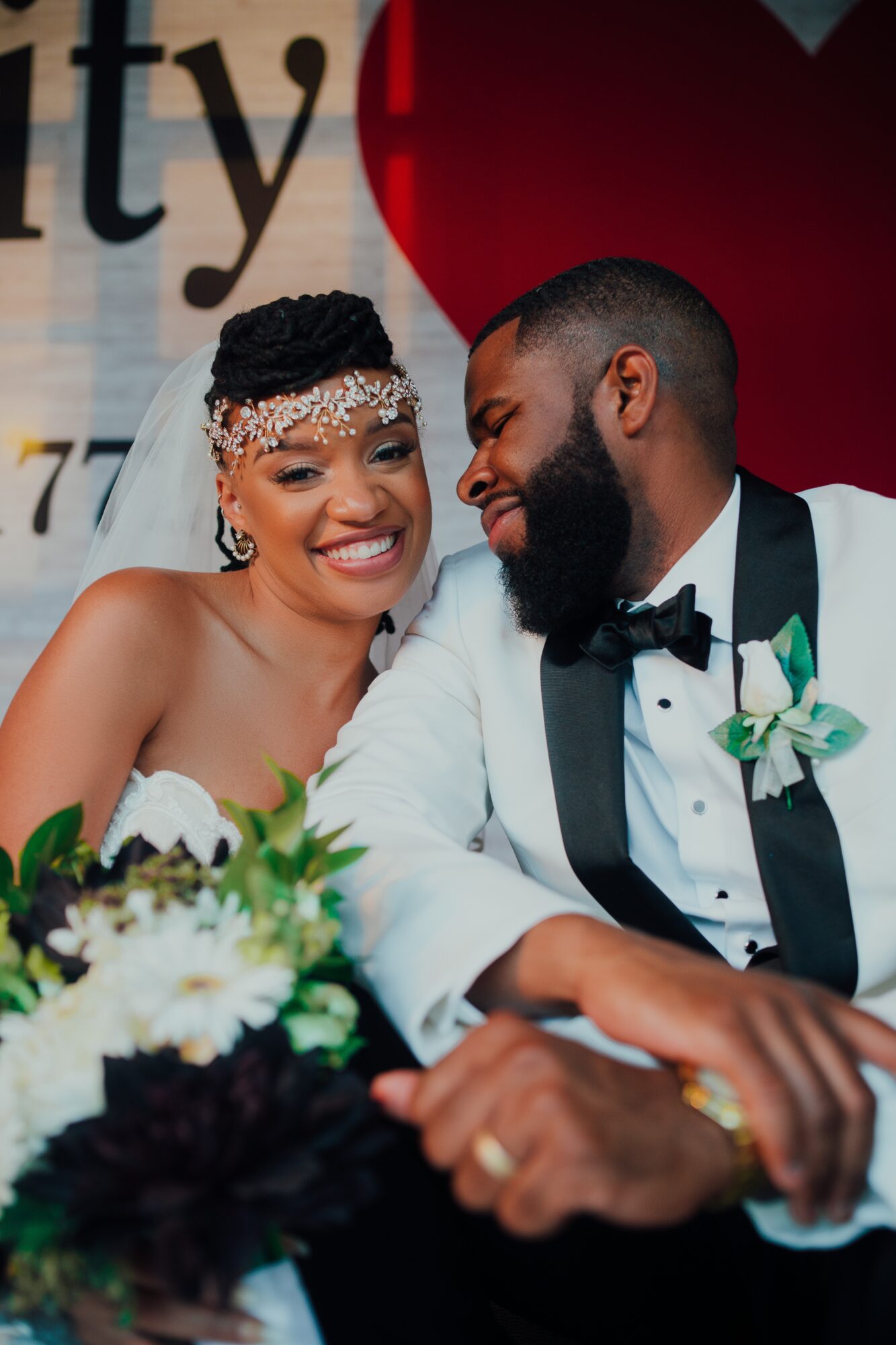 Smiling bride and groom holding hands at wedding reception, bride wearing headpiece, groom in tuxedo with boutonniere.