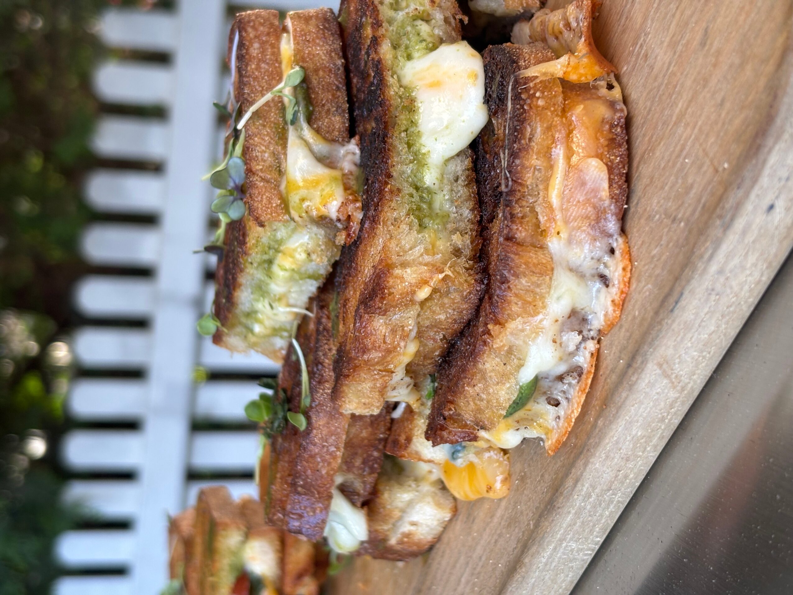 Three sandwiches with bacon, cheese, and vegetables on a wooden surface, viewed sideways.
