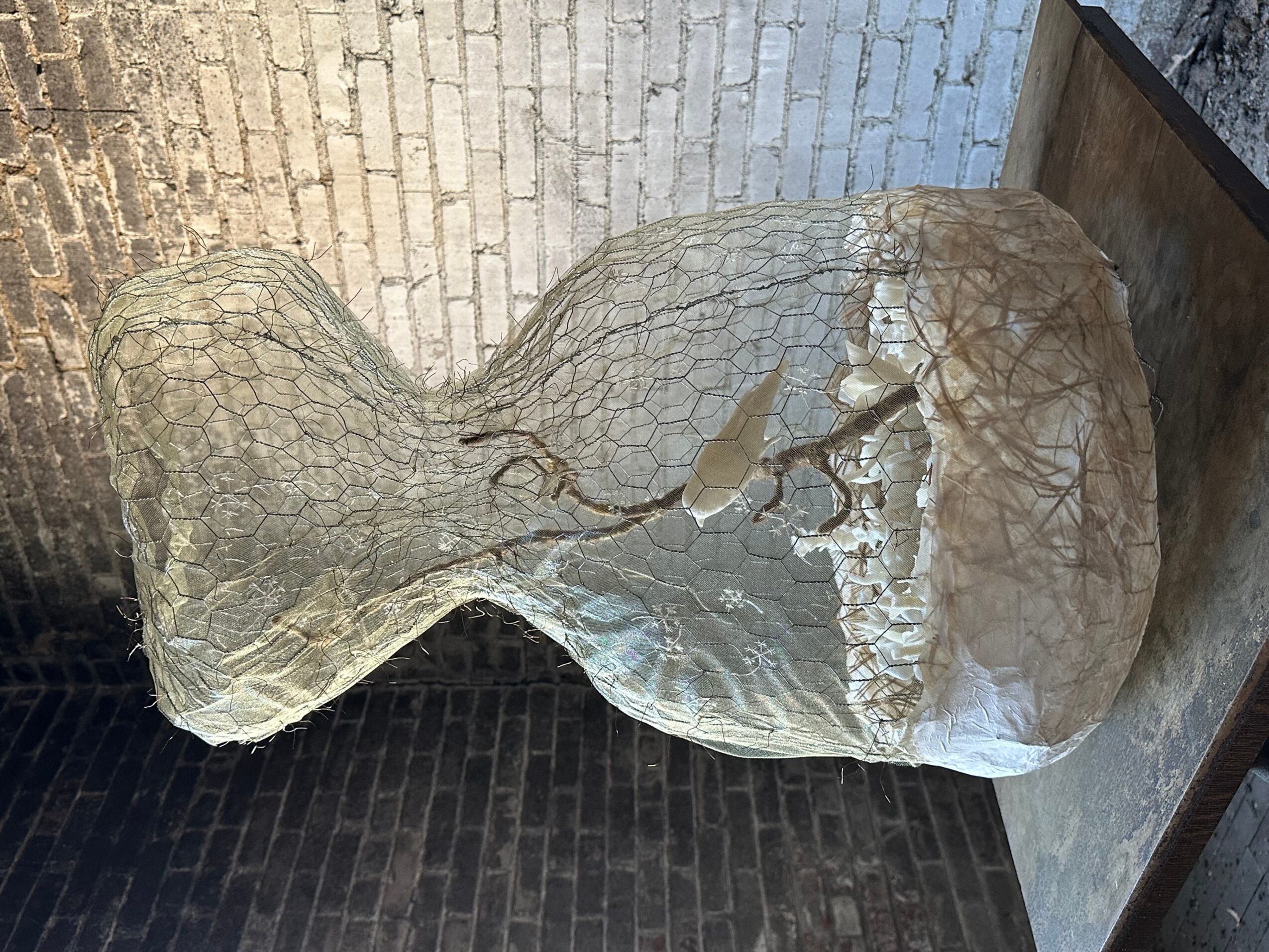A large, irregularly shaped stone with a rough surface, placed on a dark floor and leaning against a wall.