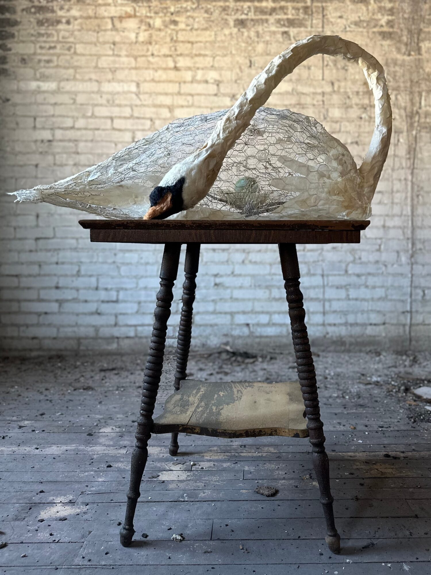 A swan sculpture on a wooden table with a brick wall background.