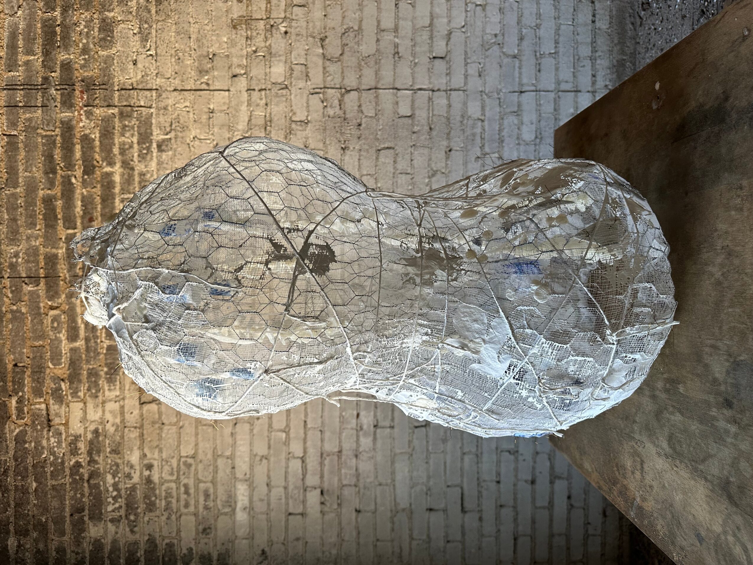 A large, irregularly shaped ice sculpture on a concrete surface, with a brick wall in the background.