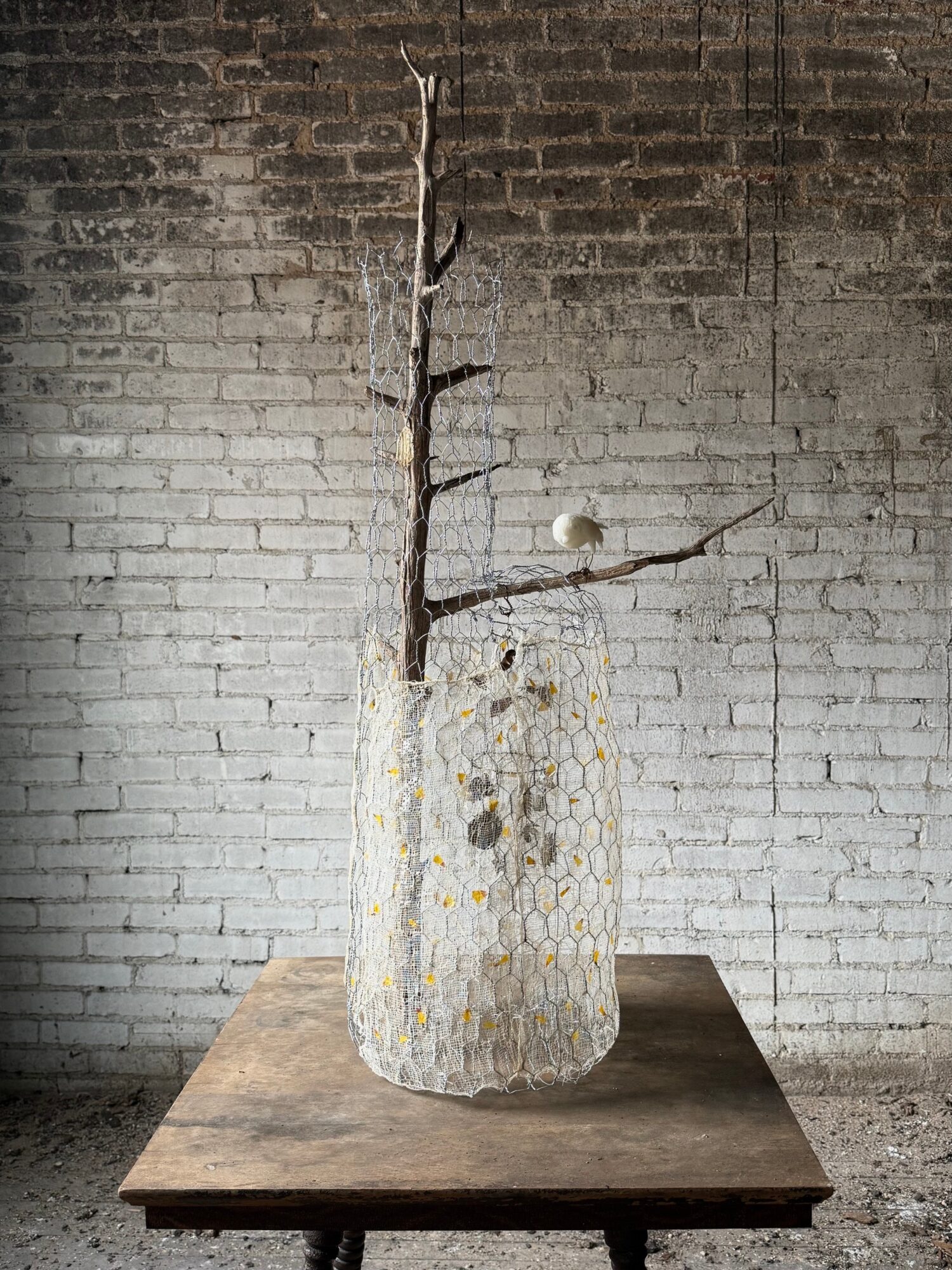 Decorative vase with a branch and a small sphere on a wooden table against a brick wall, minimalistic style.