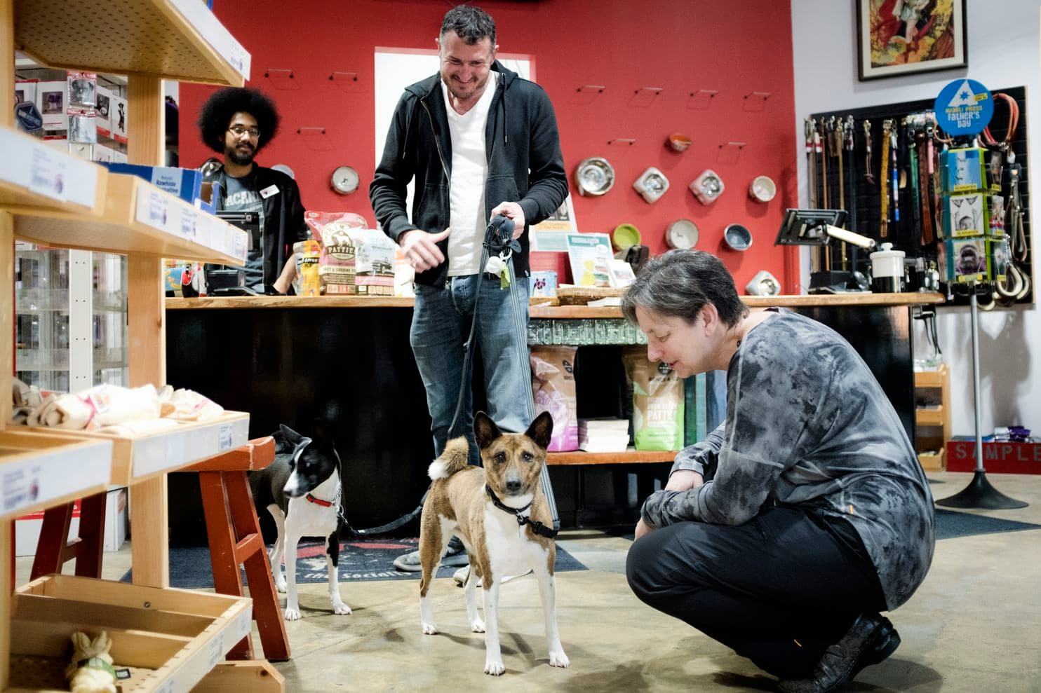 Three people and a dog inside a store, with shelves and merchandise in the background.