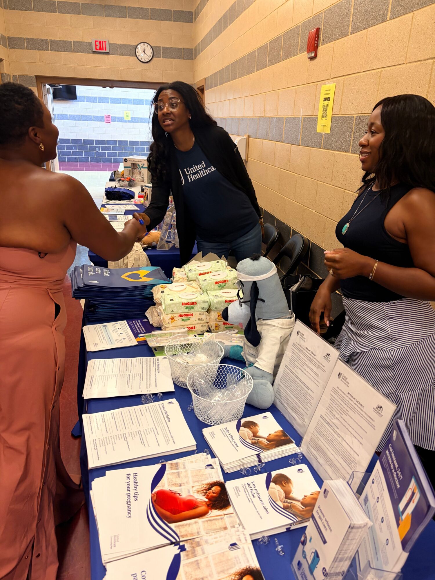 Two women at a table with informational brochures and health-related items, engaging in conversation indoors.