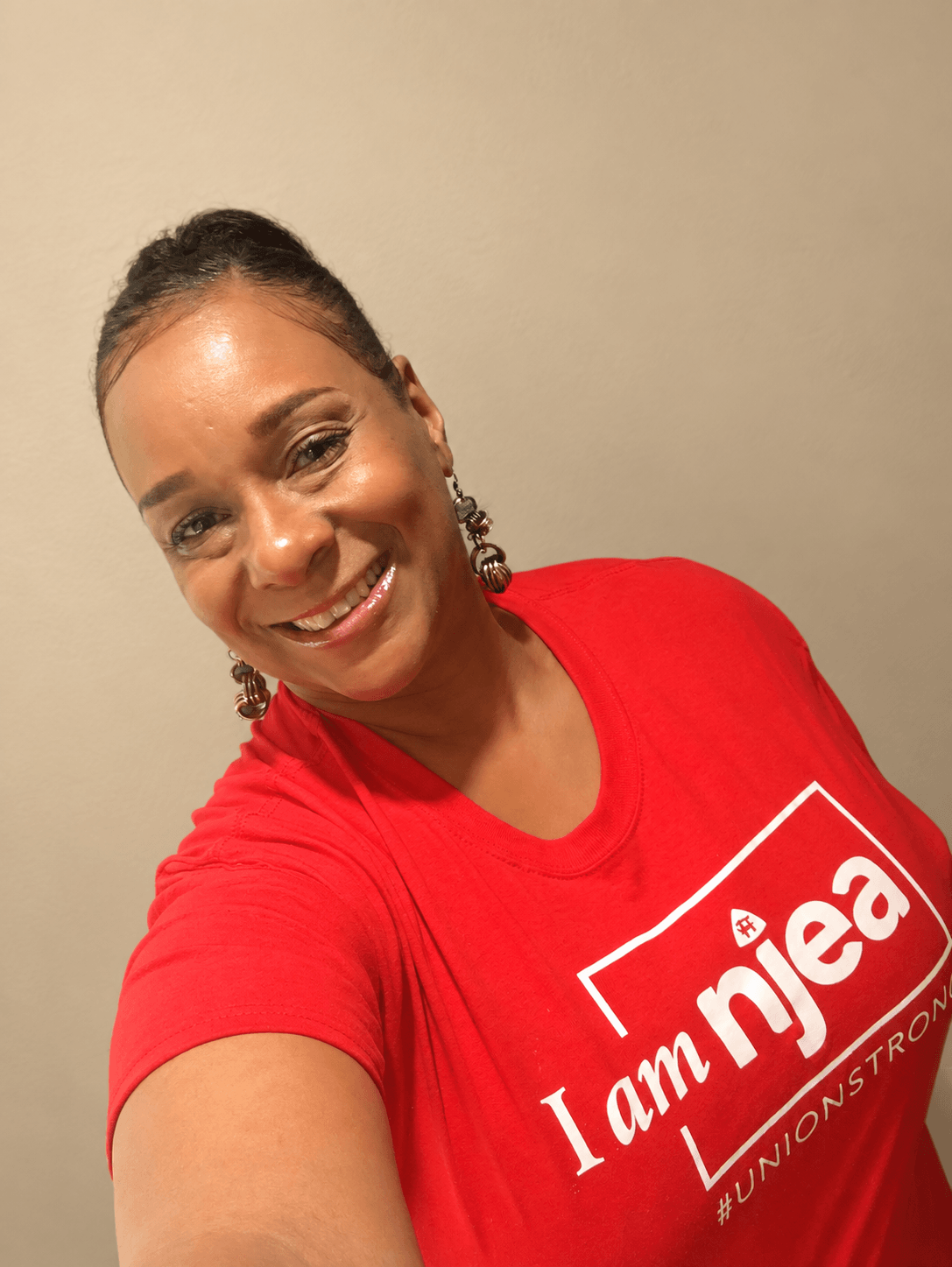 Smiling woman with earrings wearing a red T-shirt with white text, against a plain background.