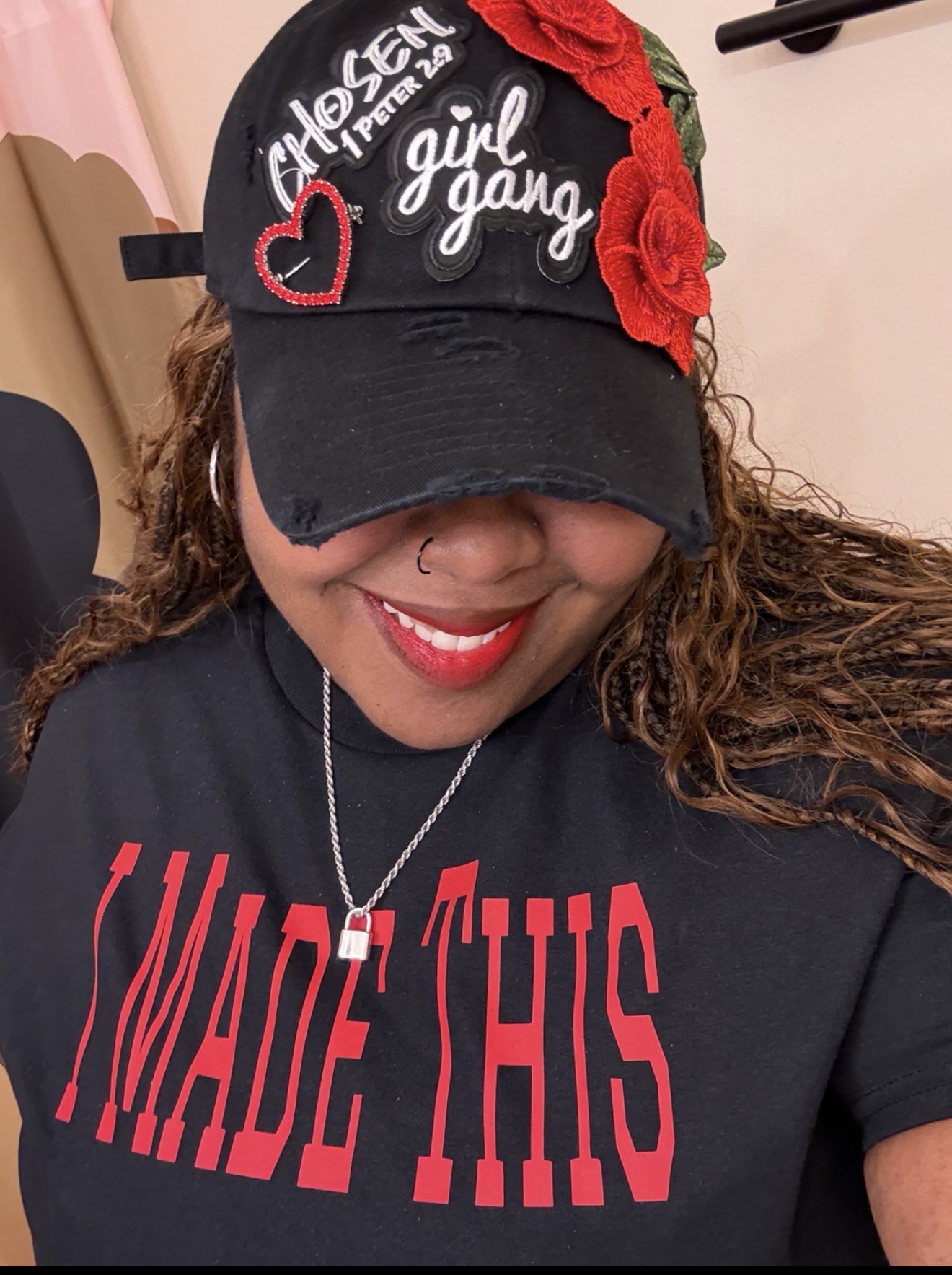 Smiling woman wearing a black cap with red roses and heart embellishments, and a black T-shirt with red text.