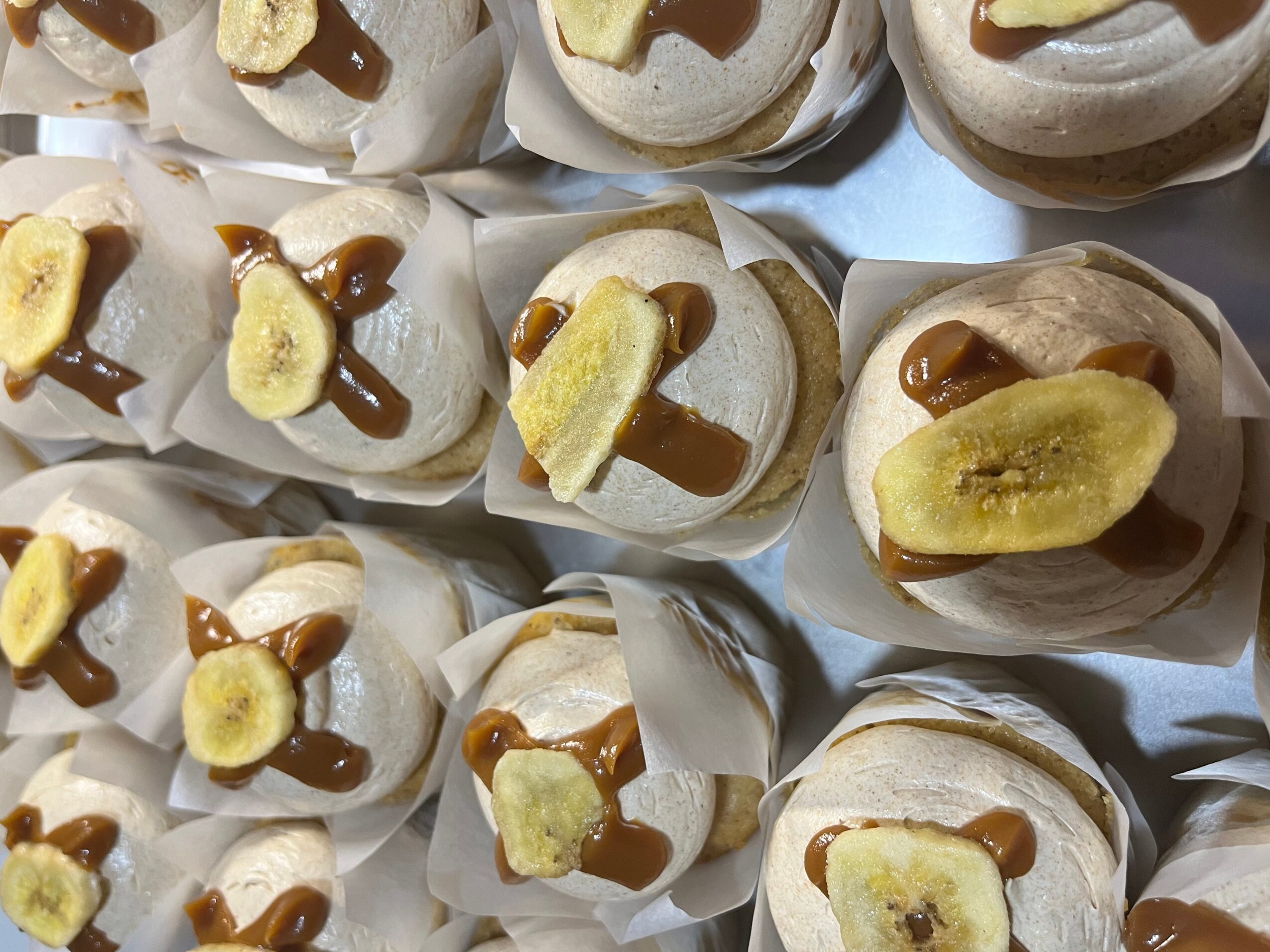 Close-up of baked goods topped with banana slices and drizzled with caramel sauce, arranged on a tray.