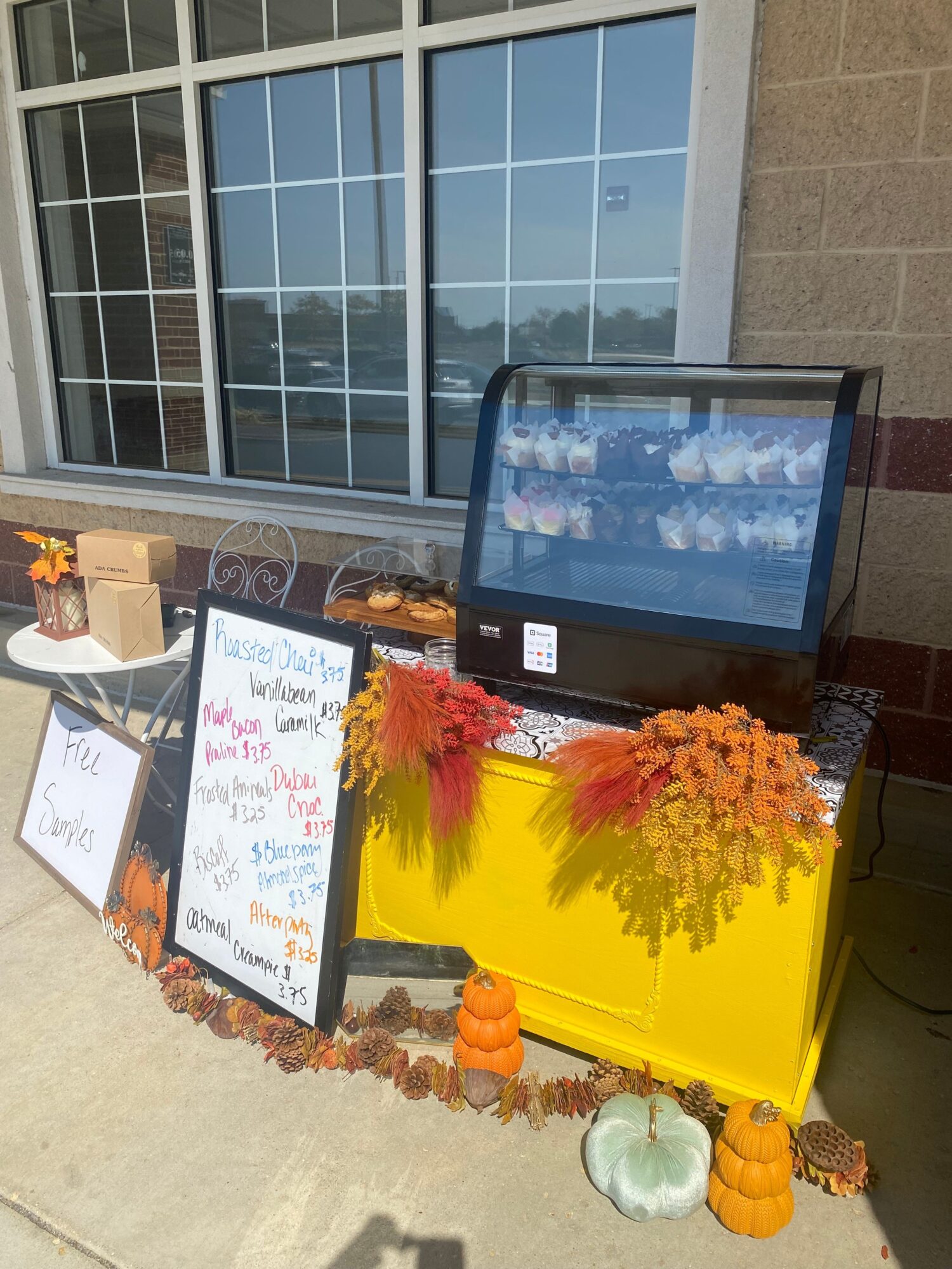 A display with a yellow container, pumpkins, and autumn decorations, with a whiteboard and a window in the background.